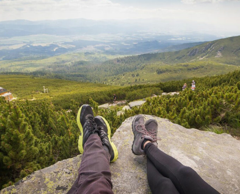 Zwei Menschen - man sieht nur die Wanderschuhe - sitzen auf einem Berg mit Blick in die Weite der Landschaft - dafür braucht es Motivation und Volition
